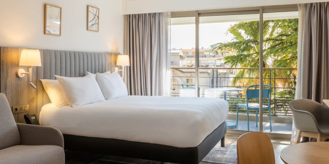 Bright hotel room with balcony overlooking trees
