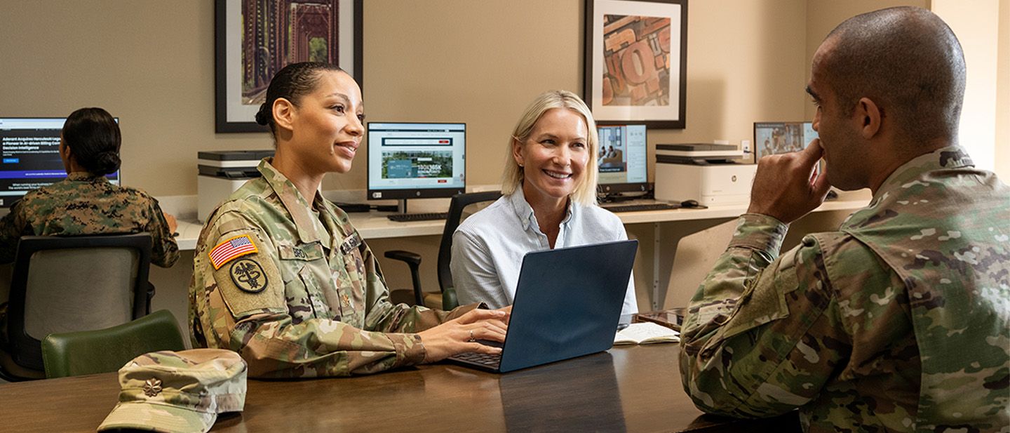 Military and civilians in hotel business center, working on desktop and laptop.