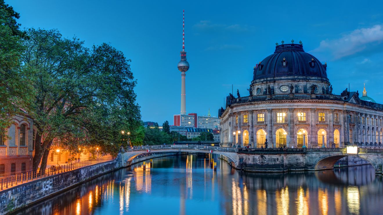 Berlin's riverside buildings illuminated at night, reflected on the water
