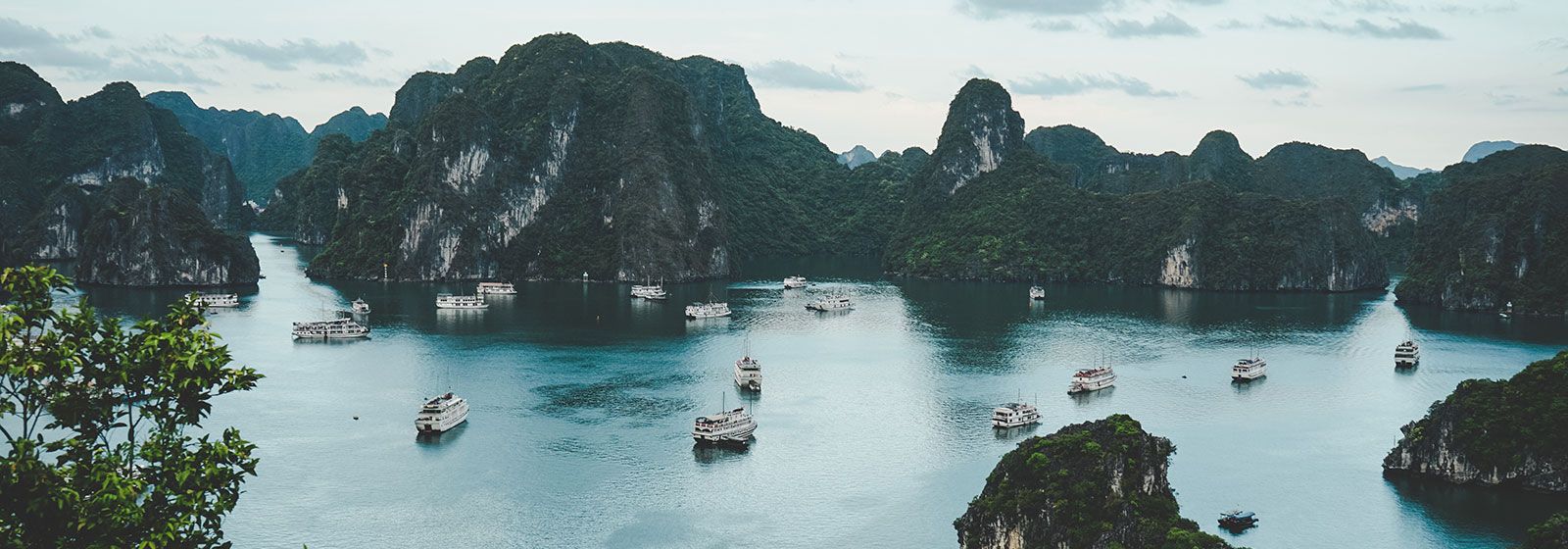 Boats meandering the waters of Ha Long Bay surrounded by tall cliffs