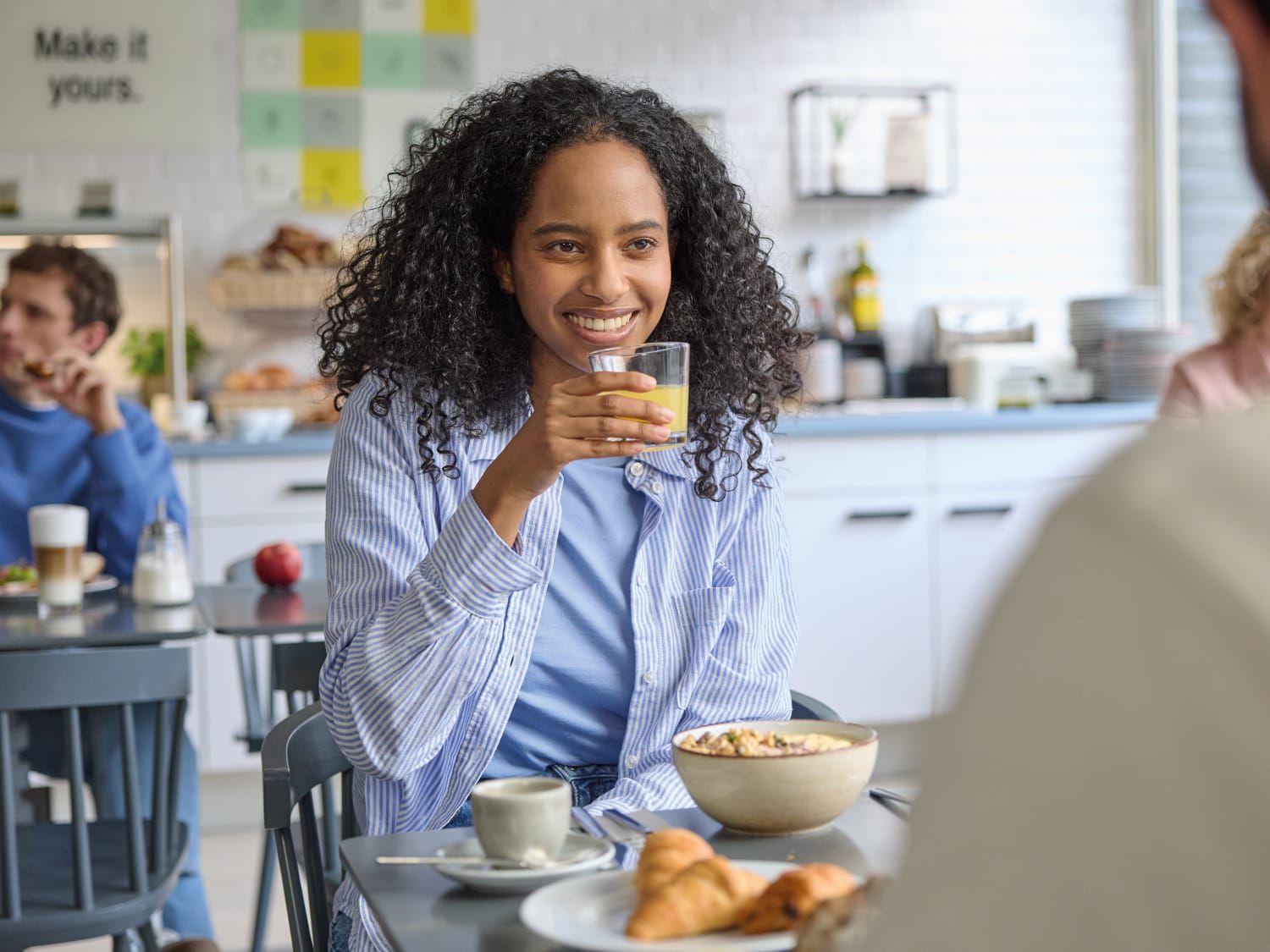 A woman with long curly hair enjoying a hot in-hotel breakfast.