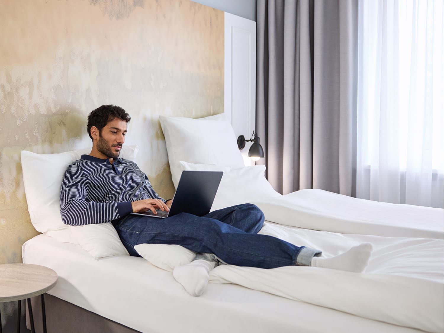 A young man relaxing in his plush bed with a laptop.