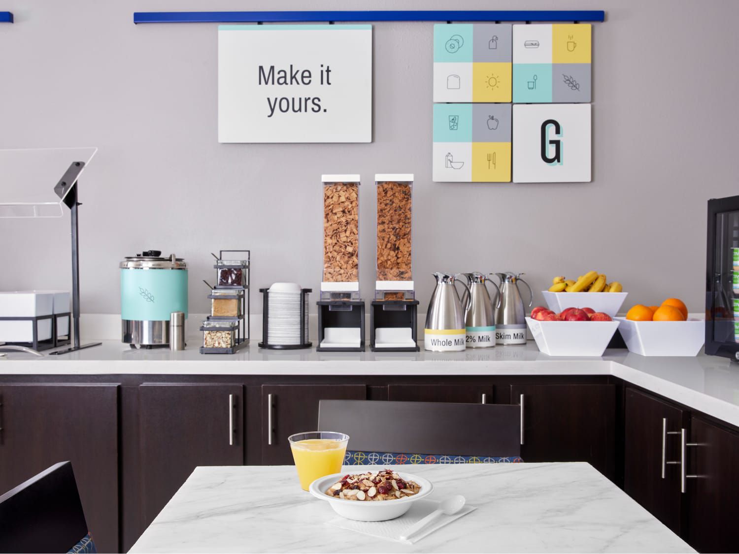 Hotel breakfast bar with cereal, fruit, milk, and a “Make it yours” sign.