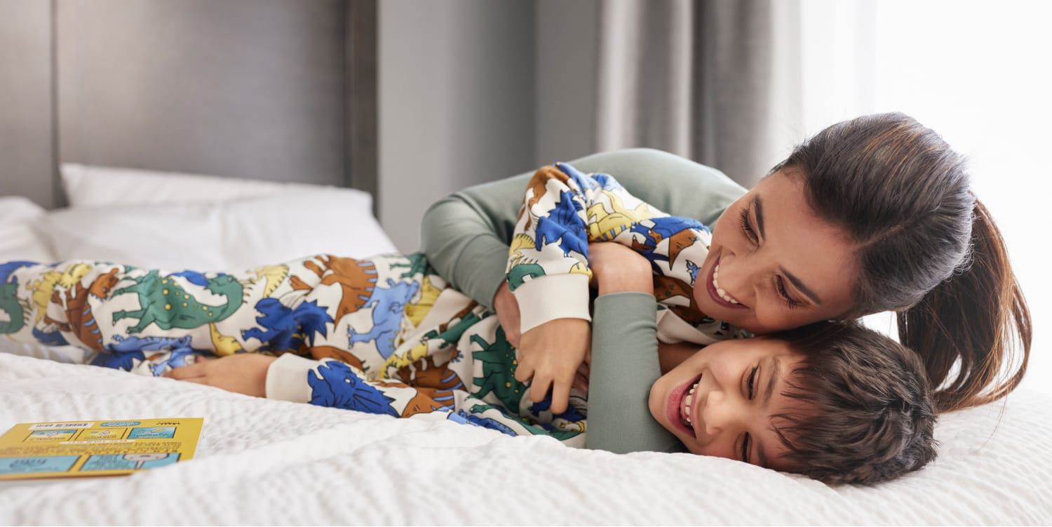 Mother and young son laughing on comfortable hotel bed