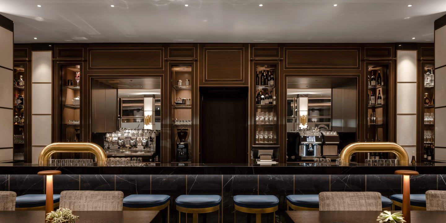 Elegant hotel bar with dark wood, marble counter, and seating.