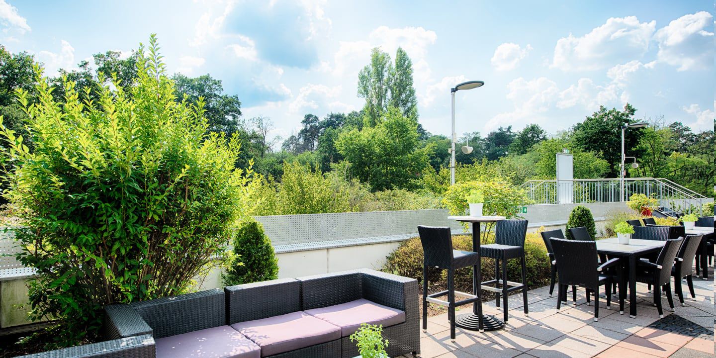 Outdoor patio with wicker seating, dining tables, and greenery.
