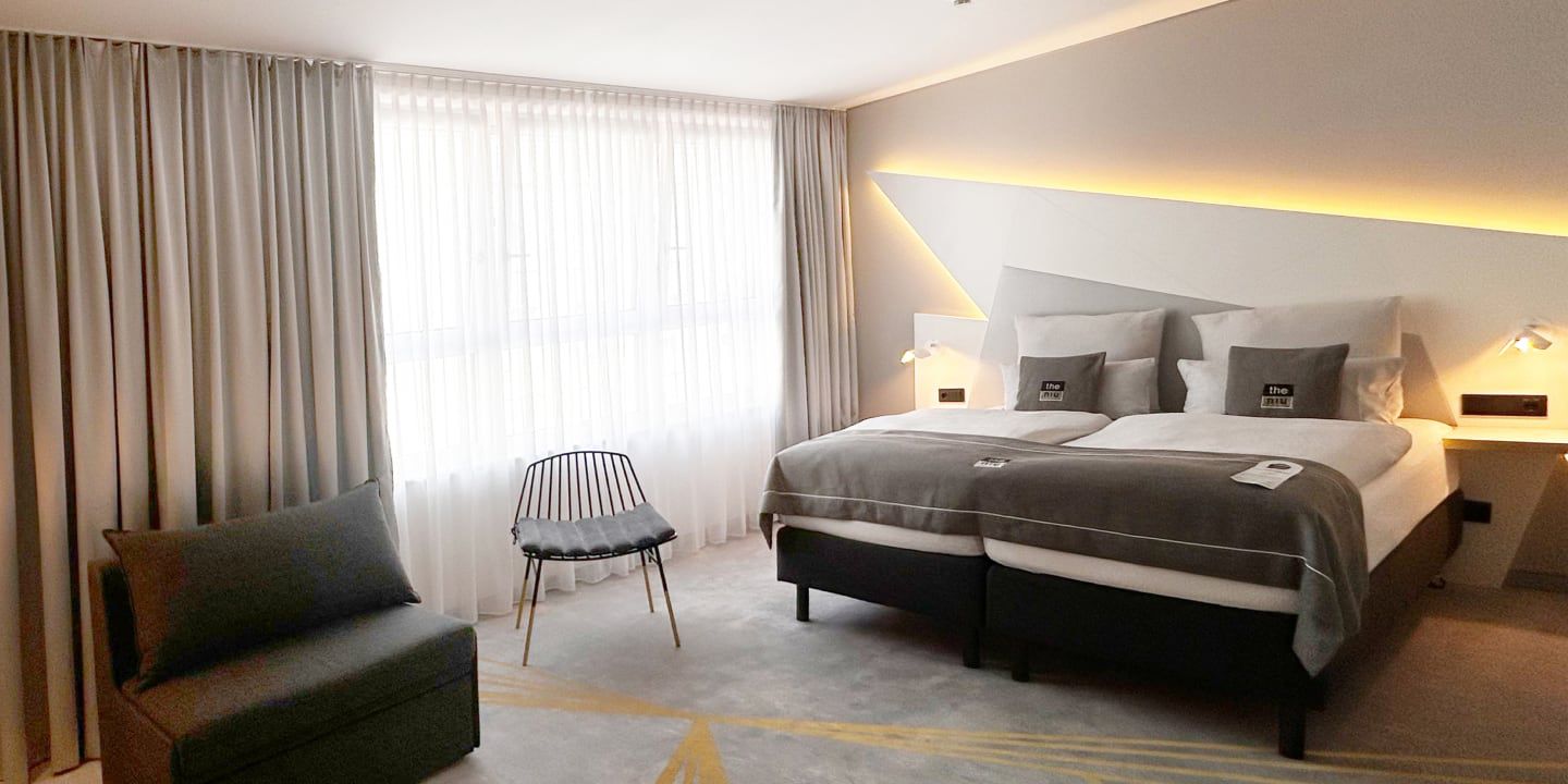 Modern hotel room with twin beds, gray decor, and soft lighting.