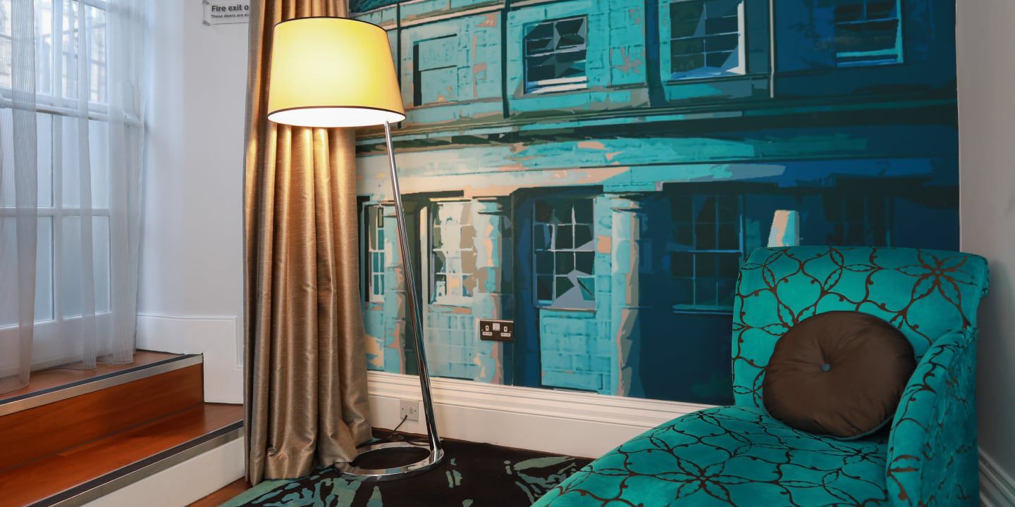 Hotel room with a teal armchair, floor lamp, and a large mural depicting street scene