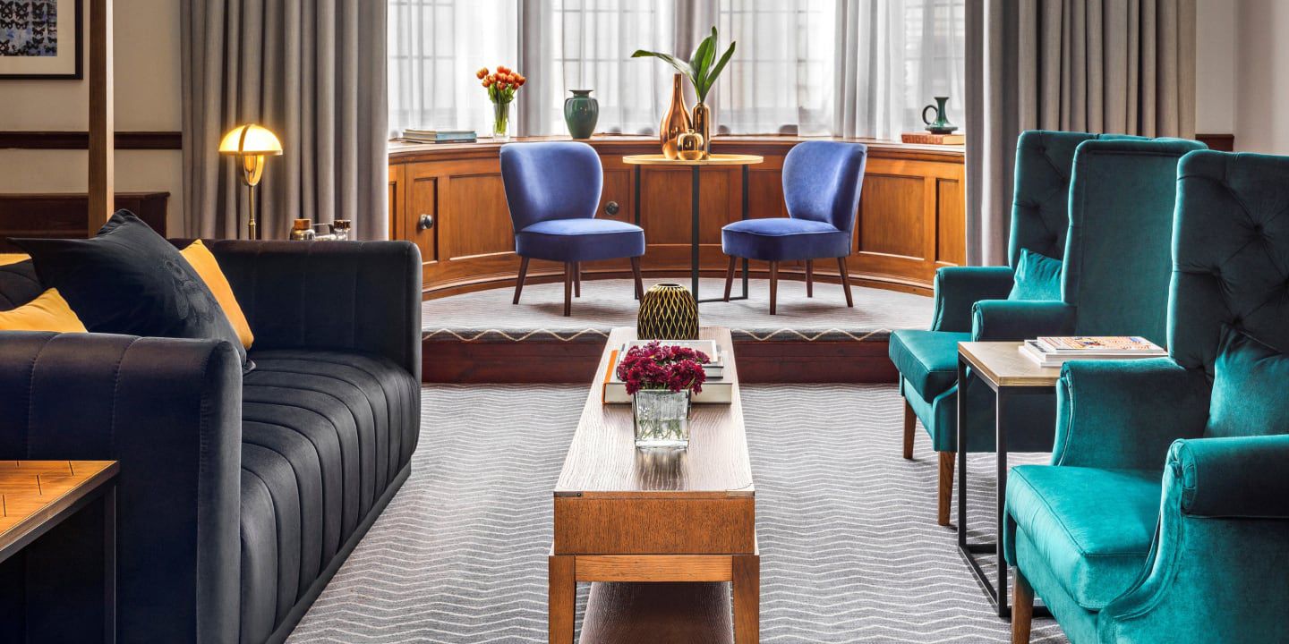 Modern lounge with blue and teal chairs, sofas, and tall windows.