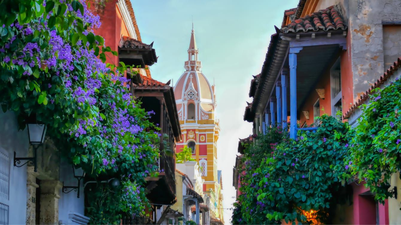 Colorful Cartagena street with flowering vines and a church tower in the background.