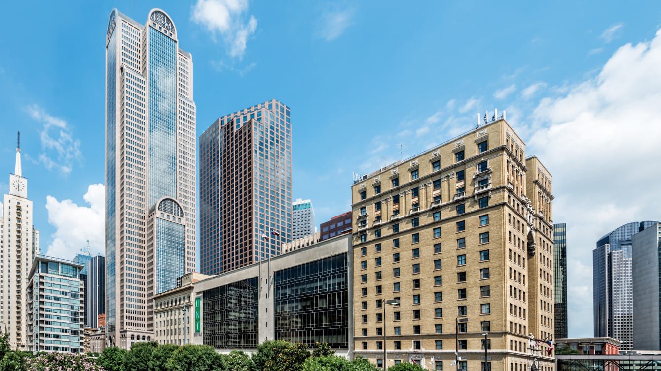 Downtown Dallas buildings and high-rise towers under a bright blue sky.
