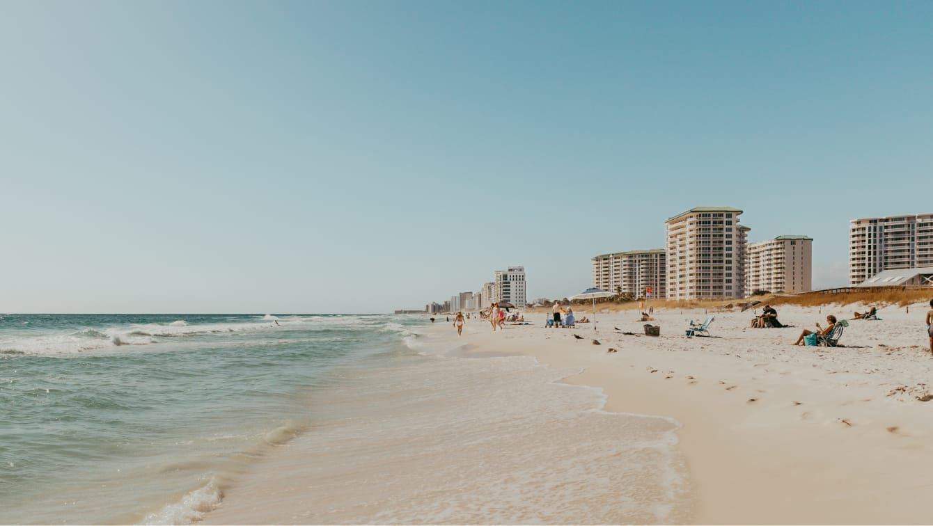 Sandy beach with gentle ocean waves and beachfront buildings in the distance.
