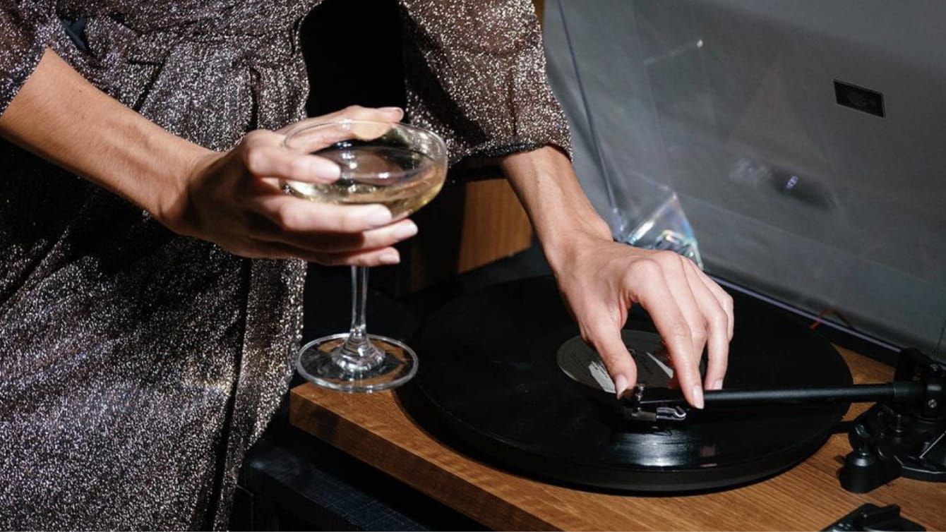 One hand on a cocktail and the other dropping the needle on a record.