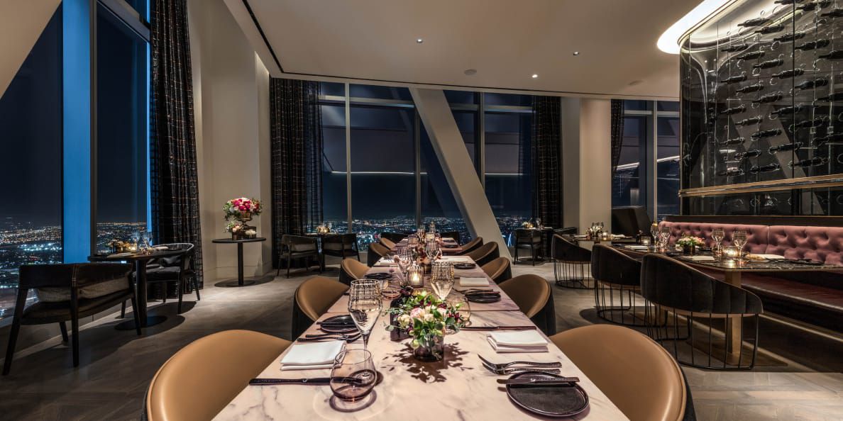 A glamorous dining room with a wine wall and floor-to-ceiling windows overlooking the city at night.