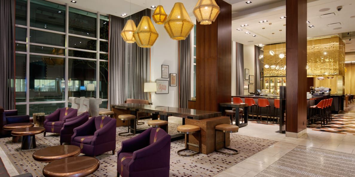 A grand lounge and bar space with aubergine and orange seating and diamond-shaped pendant lighting.