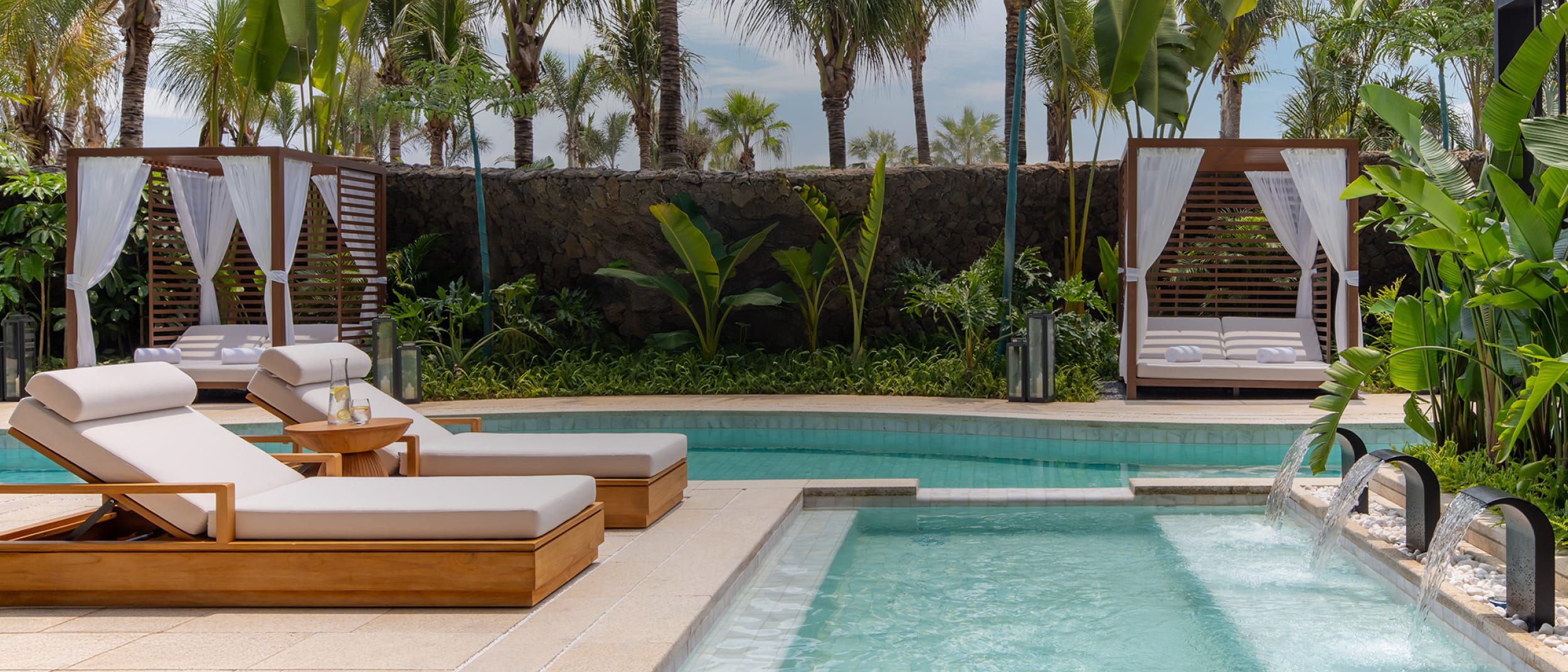 Luxury honeymoon resort pool with cabanas, loungers, palm trees, and waterfall feature at Kimpton Aeqos Hainan