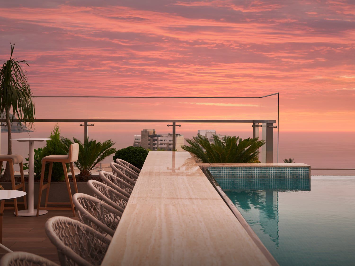 Una puesta de sol con tonos rosas sobre el agua vista desde el comedor y la zona de la piscina de la azotea del hotel SOUMA, Vignette Collection.