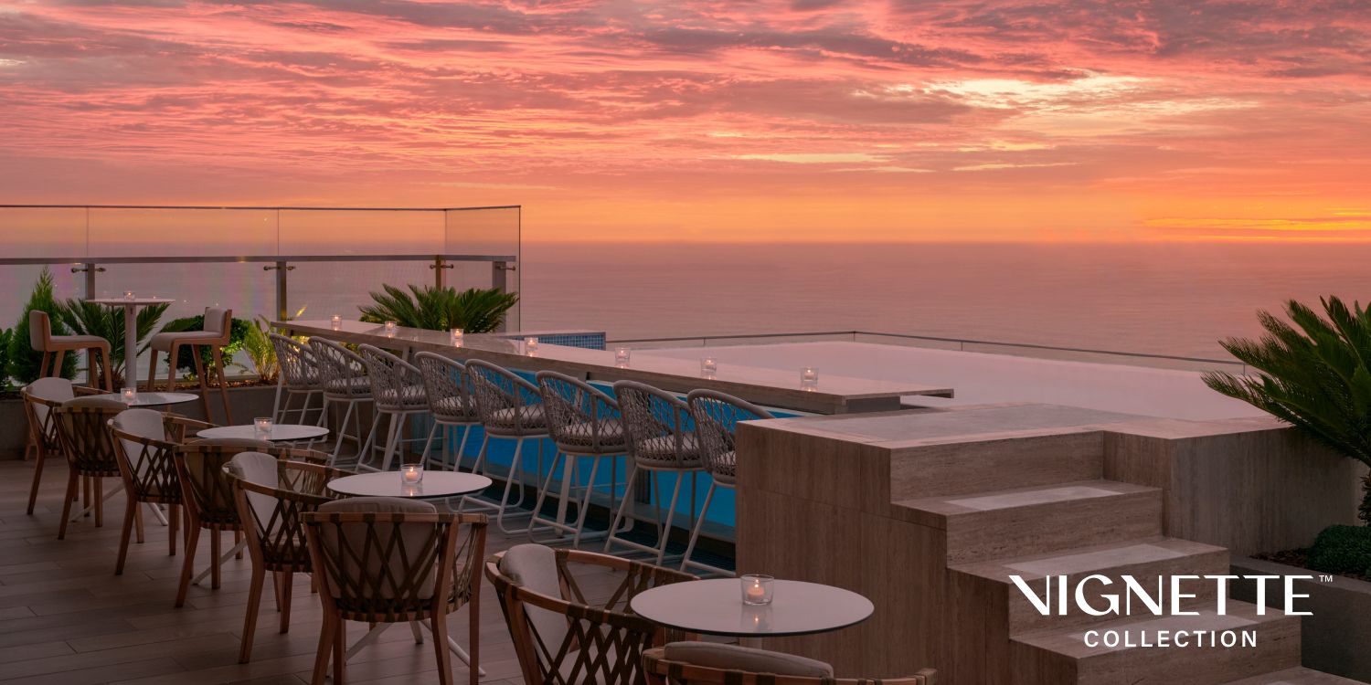 Rooftop terrace overlooking the ocean at sunset, with beautiful pink and orange sky; “Vignette Collection” logo overlaid in corner.
