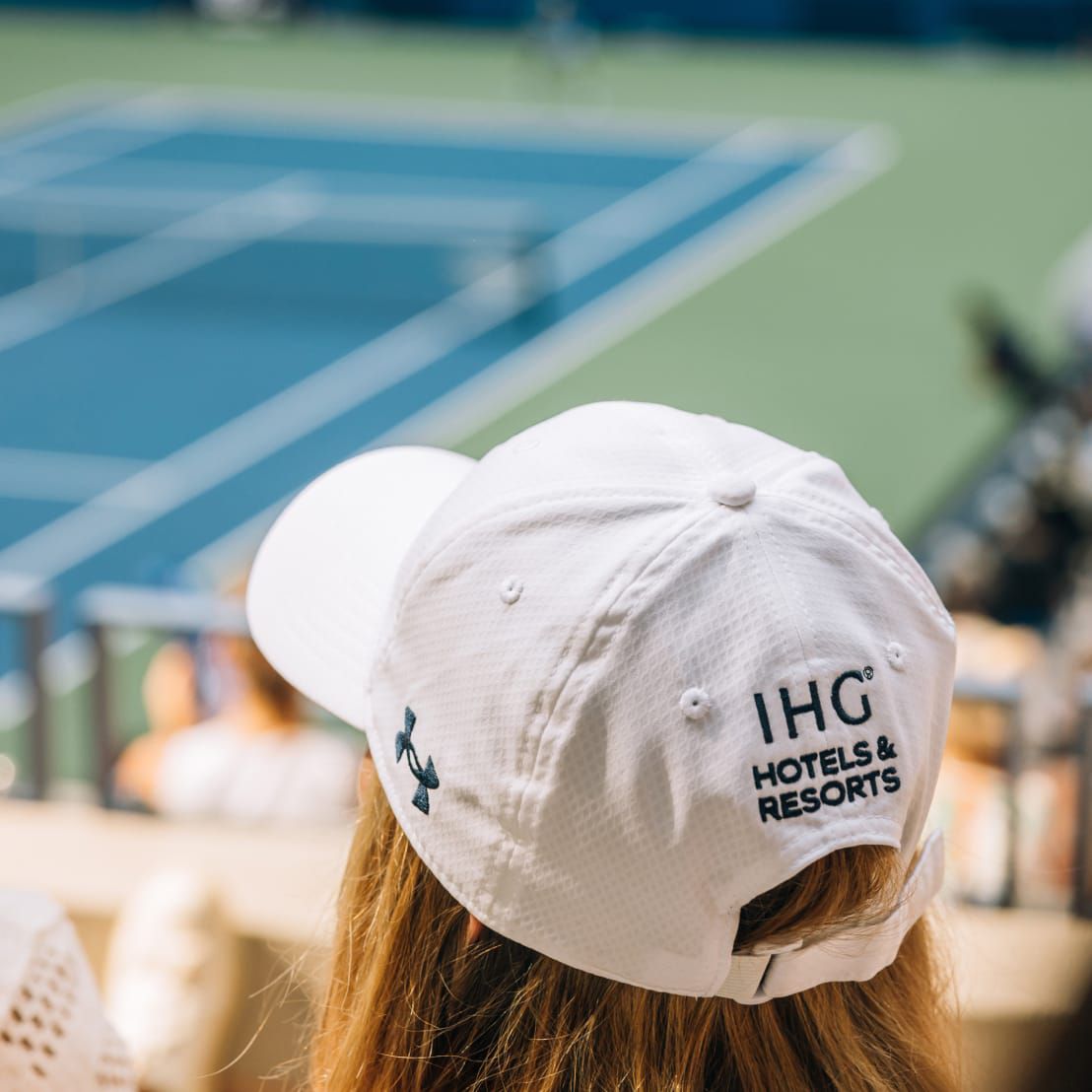 View of the back of a woman watching the match wearing an IHG Hotels and Resorts logo hat.