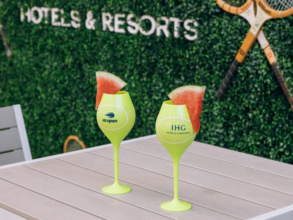 Two yellow cocktail cups with watermelon garnish and a green wall backdrop.