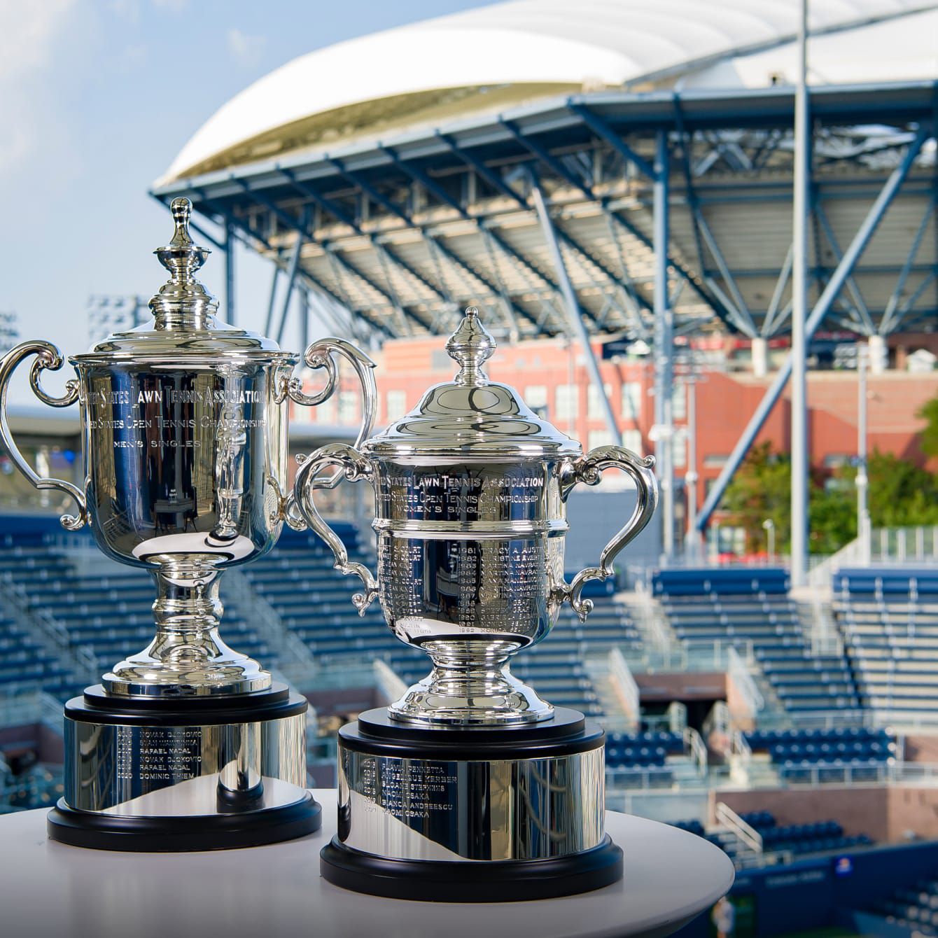 A view of two US Open Championship trophies with the stadium stands in the background.