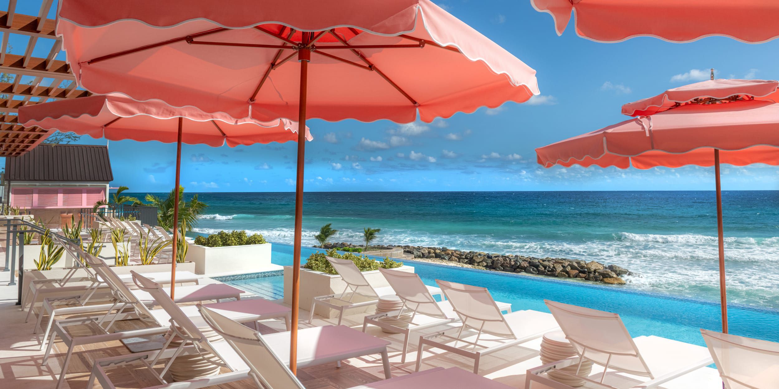 A seaside infinity pool flanked by coral-colored umbrellas.