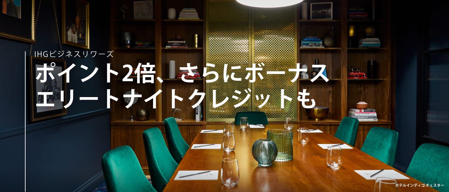 グラスが並べられたテーブルと数脚の緑色の椅子があり本棚が備え付けられている、ホテルインディゴ チェスターのミーティングルーム兼イベントスペース