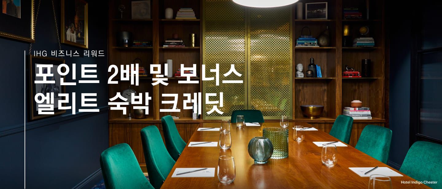 호텔 인디고 체스터의 회의실과 이벤트 공간에 책장과 초록색 의자, 유리잔이 놓인 테이블이 있습니다.