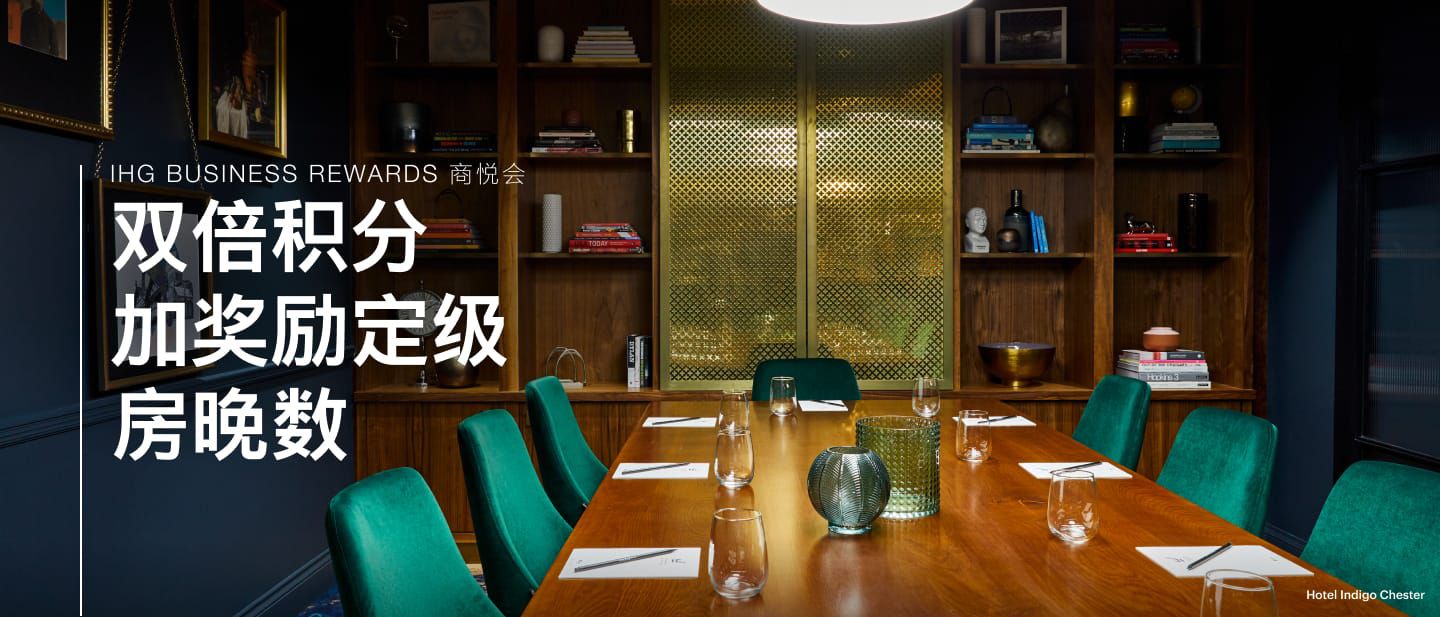 在Hotel Indigo Chester的会议室与活动空间内，有一张摆放着玻璃杯的桌子，周围配有绿色椅子，房间内还设有书架