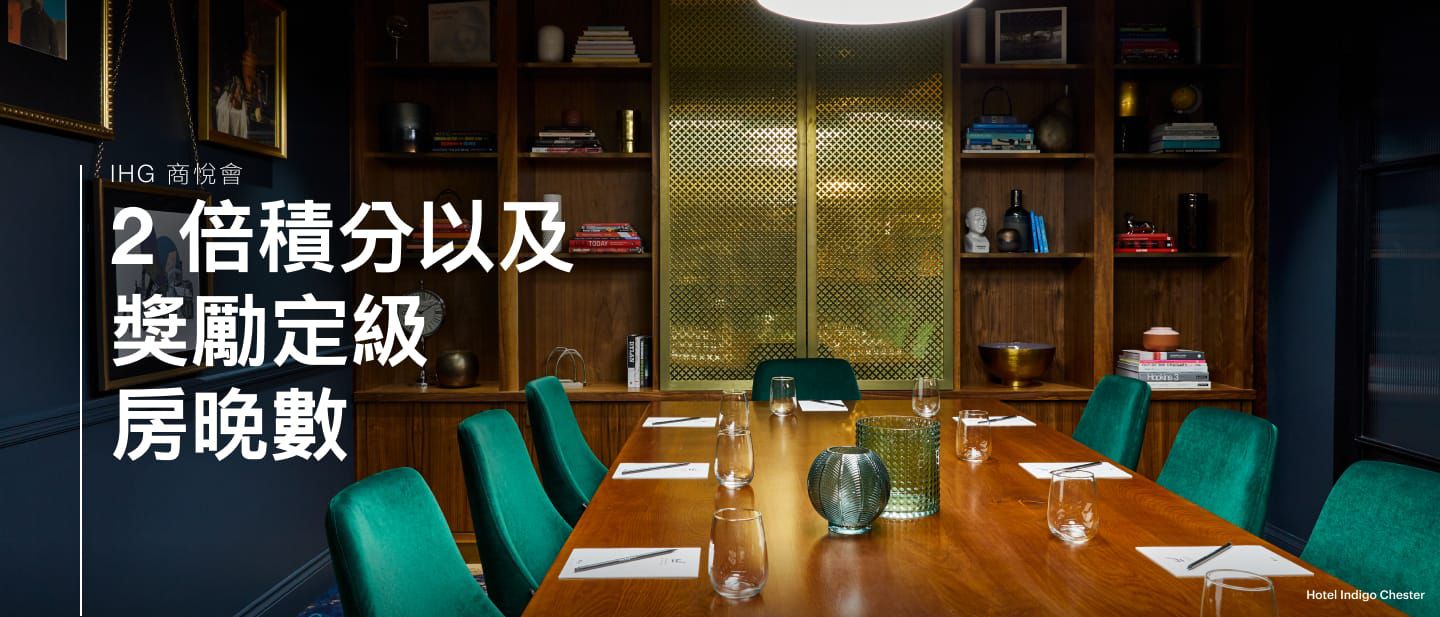 切斯特英迪格酒店的會議室和活動場地裡，有一張桌子擺放了玻璃杯、兩旁擺放了幾張綠色椅子，背景有一座書櫃