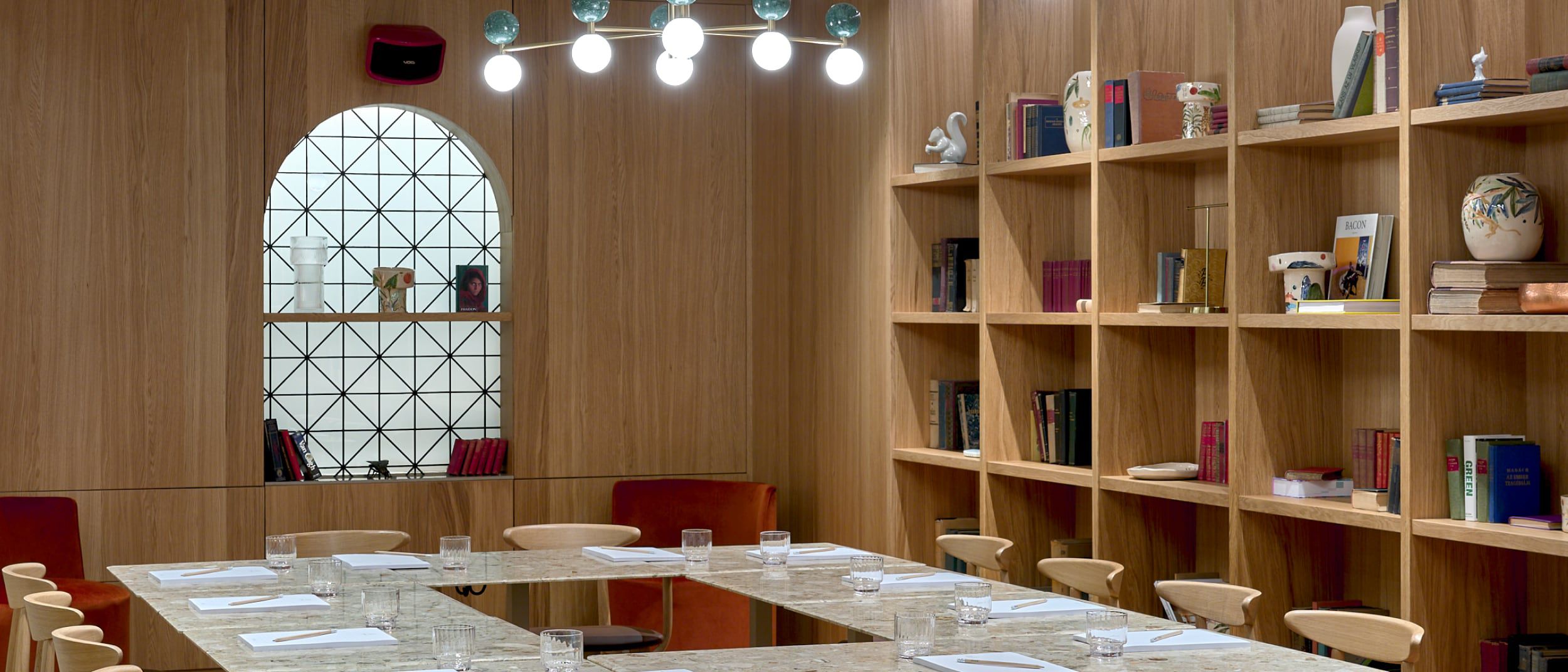 Una sala de reuniones con estilo de biblioteca, con mesa de mármol y ventanas con patrón de diamante