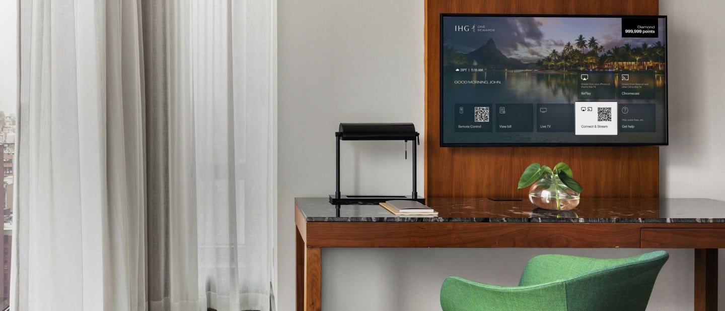 Hotel room desk and chair with a tv showing IHG menu