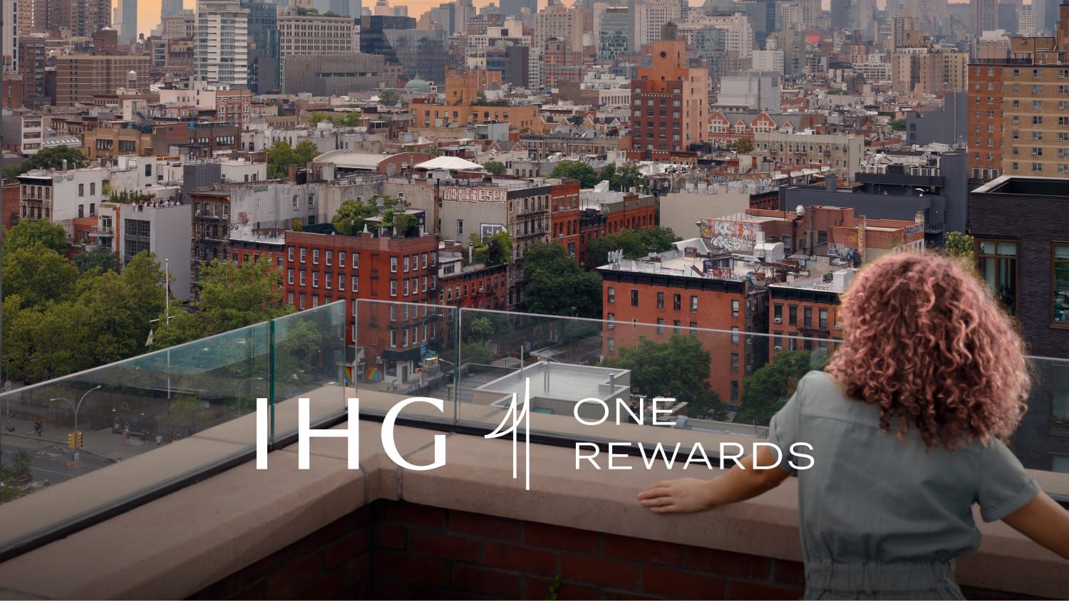 From a rooftop deck, a woman looks out over a cityscape.