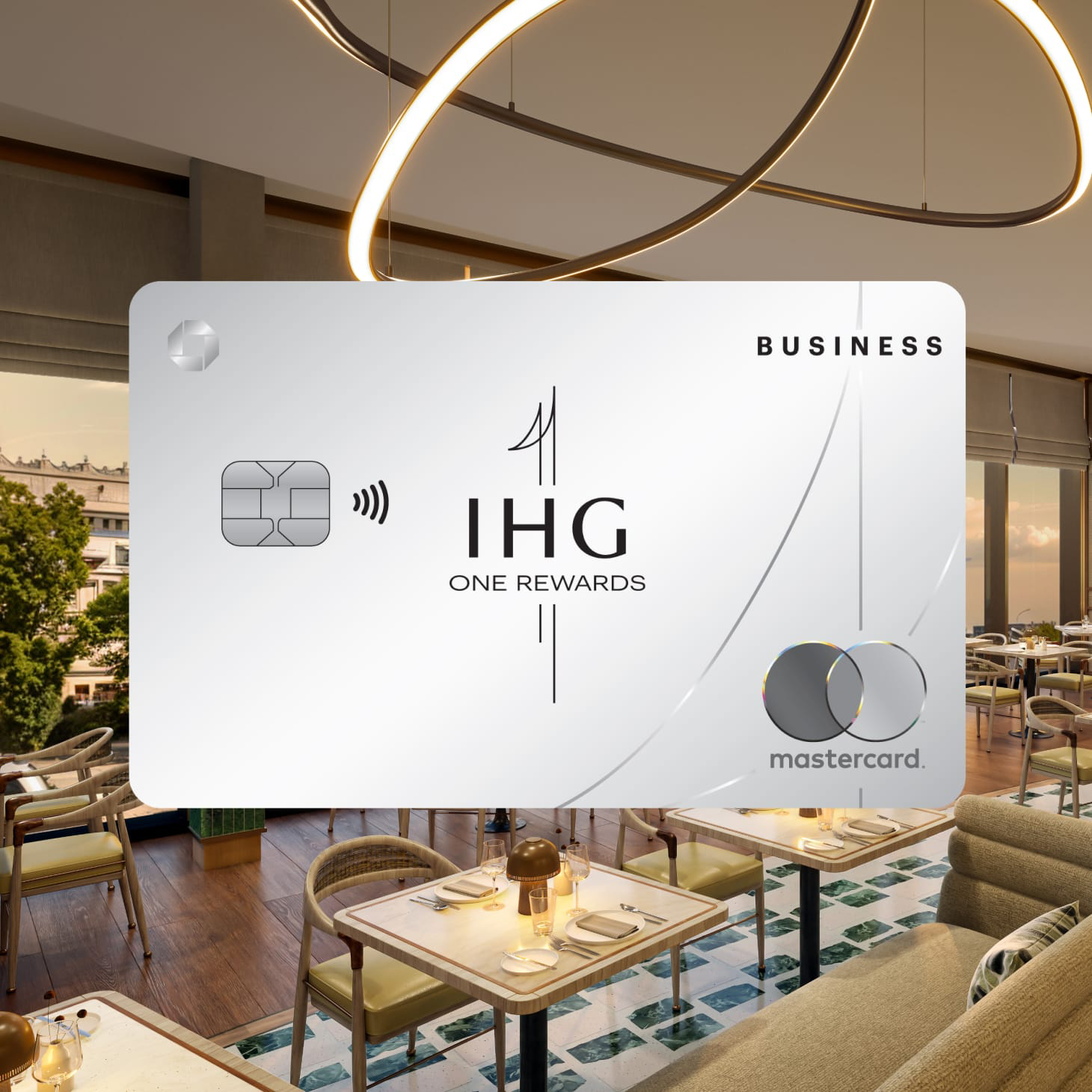 IHG One Rewards Business Credit Card overlaid on scene of an elegant restaurant with tables set.