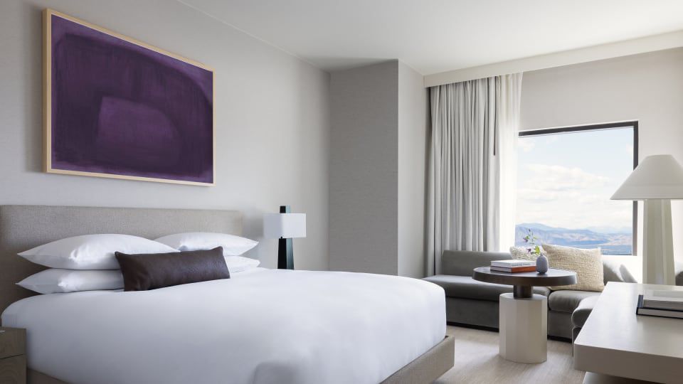 A modern guest room at the Kimpton Claret hotel featuring a white and purple interior with a plush bed