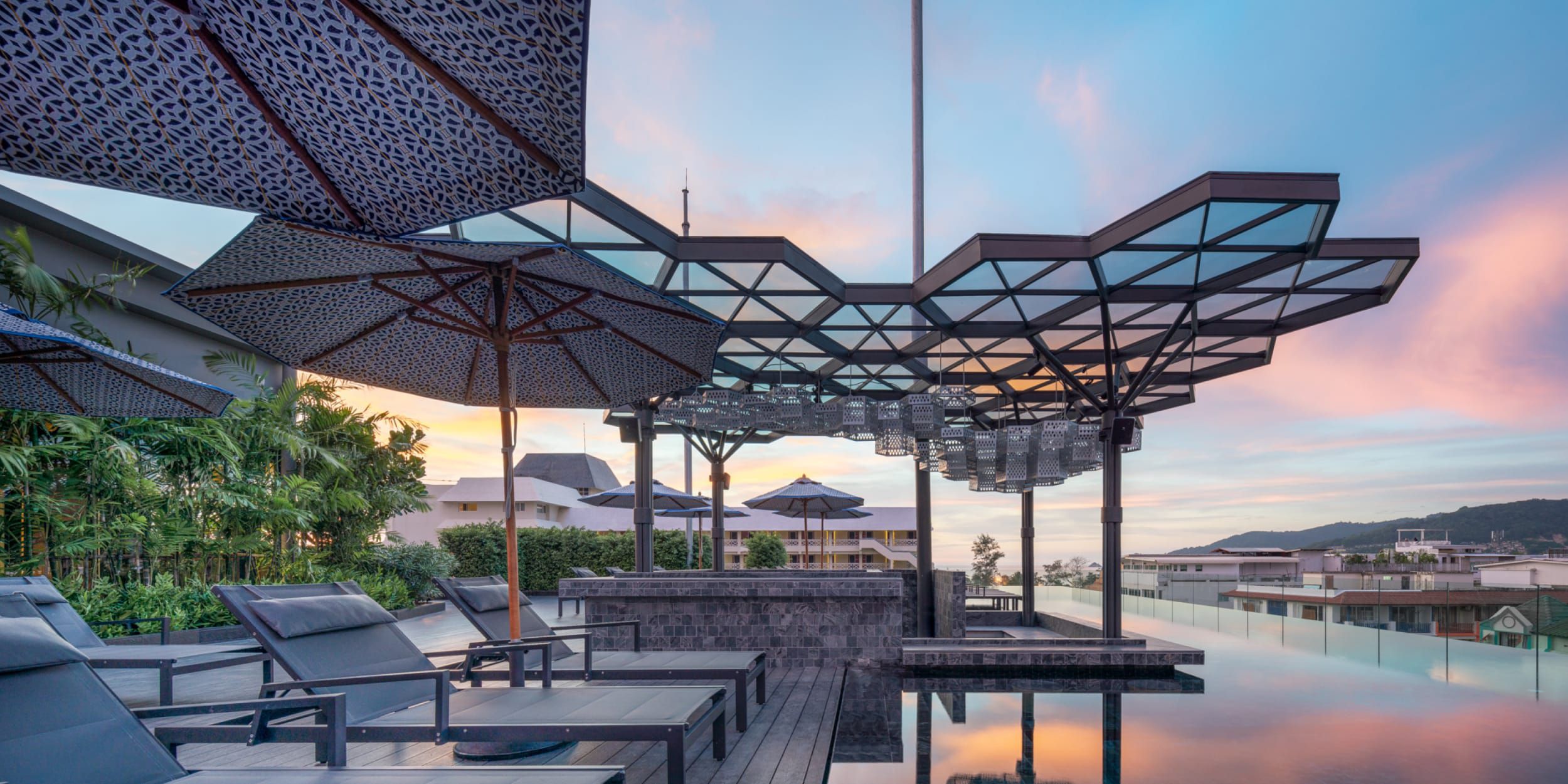 ピンク色の空が、六角形のガラスとスチールでできたキャノピーの下にある屋上プールの水面に映り込んでいる。