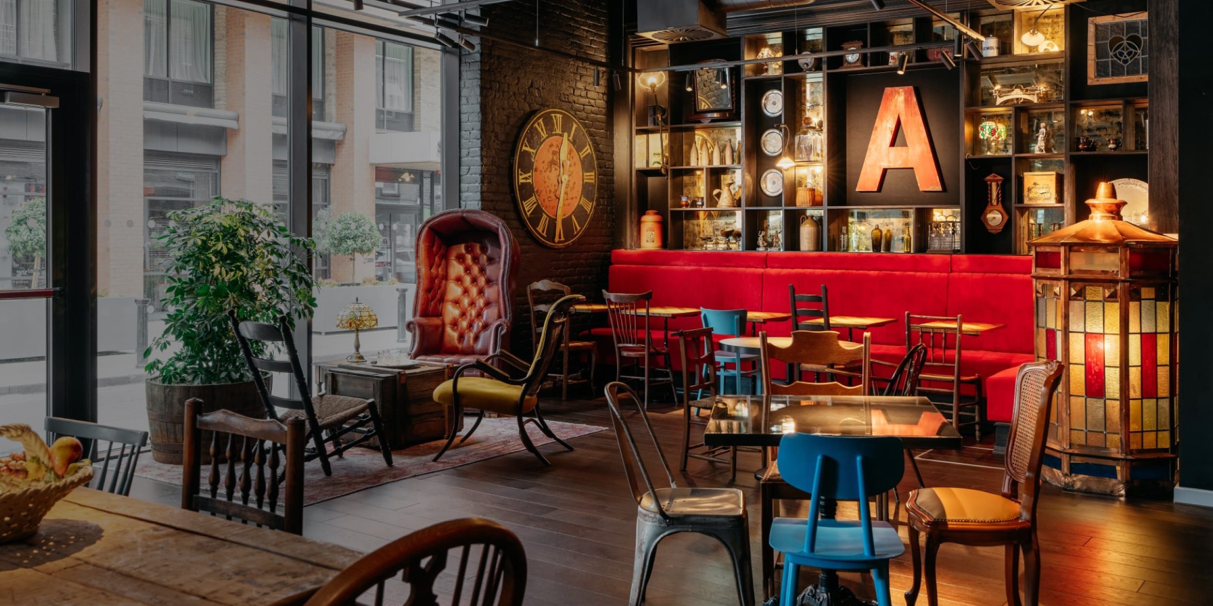 A vibrant lobby with red banquette seating, mismatched tables and chairs, and shelves of trinkets.