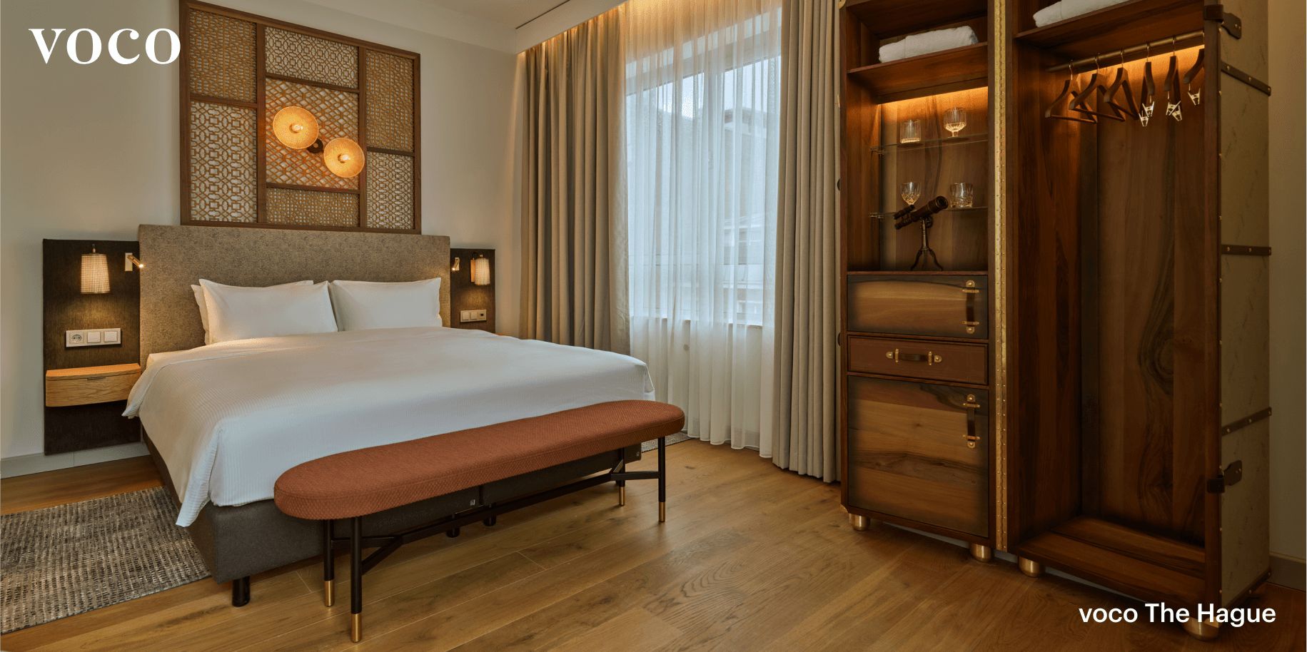  A pristine, serene king room at the voco The Hague, featuring an elegant, backlit wardrobe.