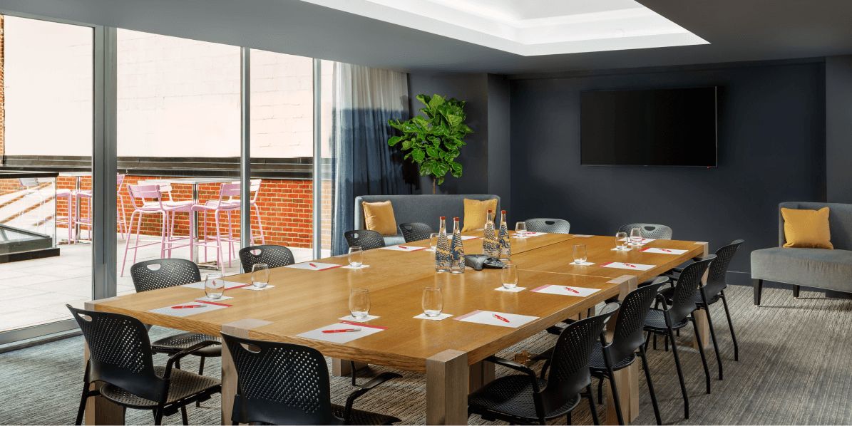 The Gallery meeting space with a wooden boardroom table, chairs and a table, with floor to ceiling windows