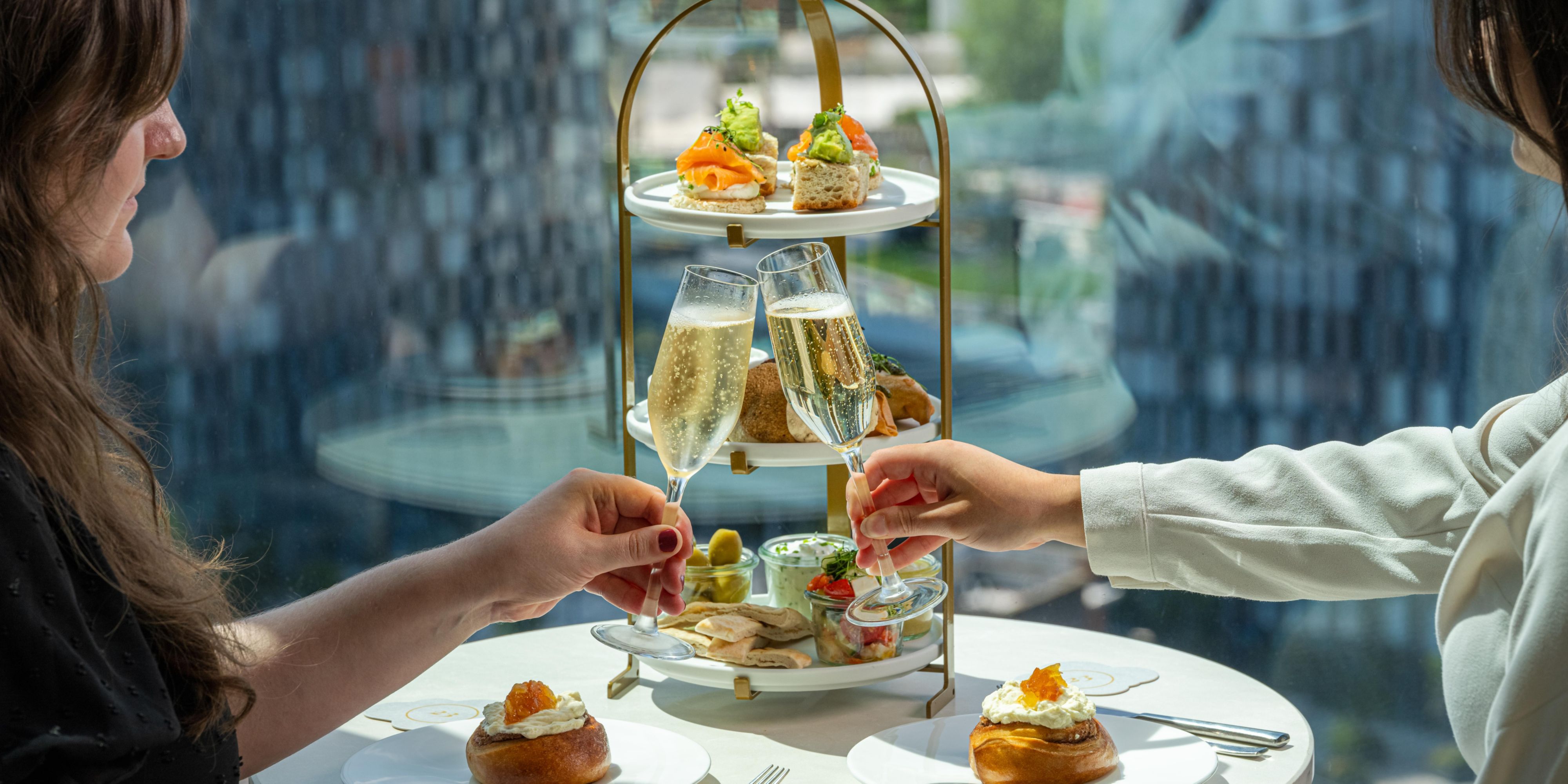 two people sitting having afternoon tea, and cheersing two glasses of prosecco