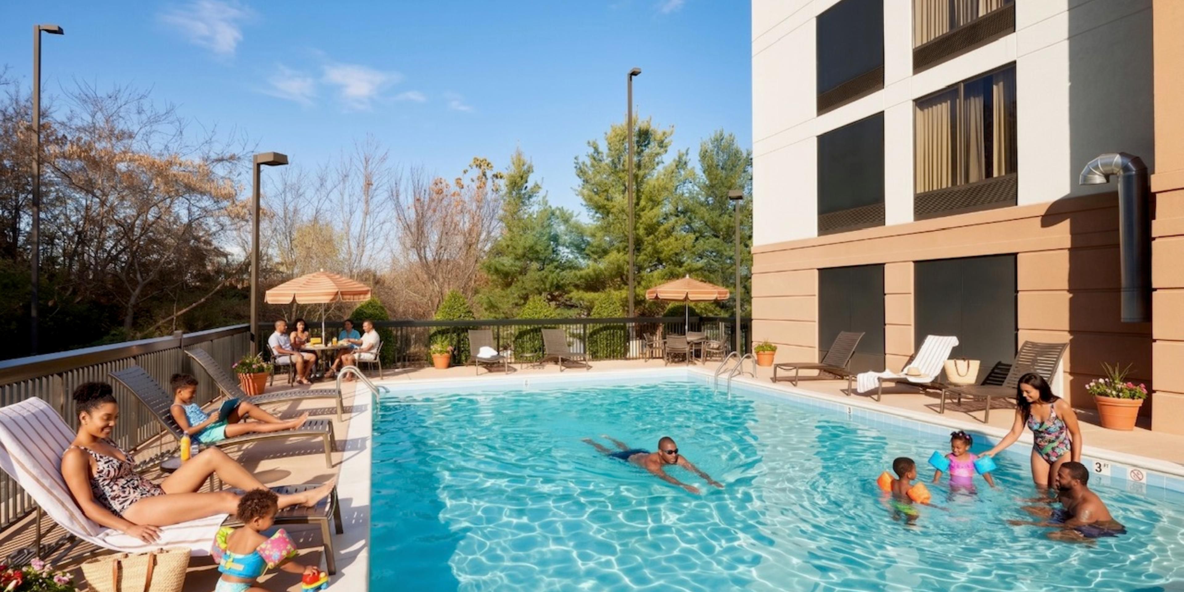 Outdoor hotel pool with lounge chairs and guests on a sunny day.