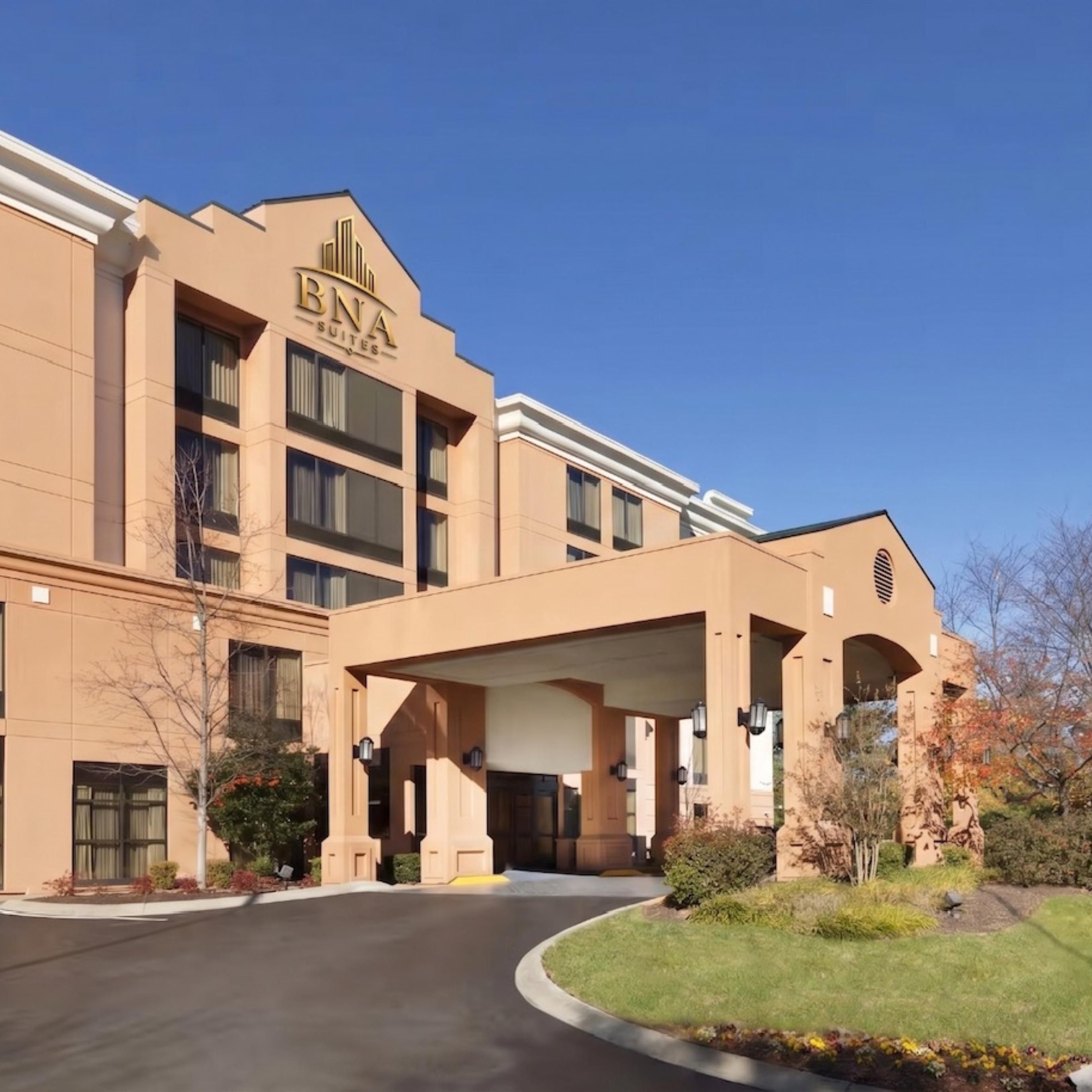 Hotel exterior with covered entrance and flagpole on clear day.