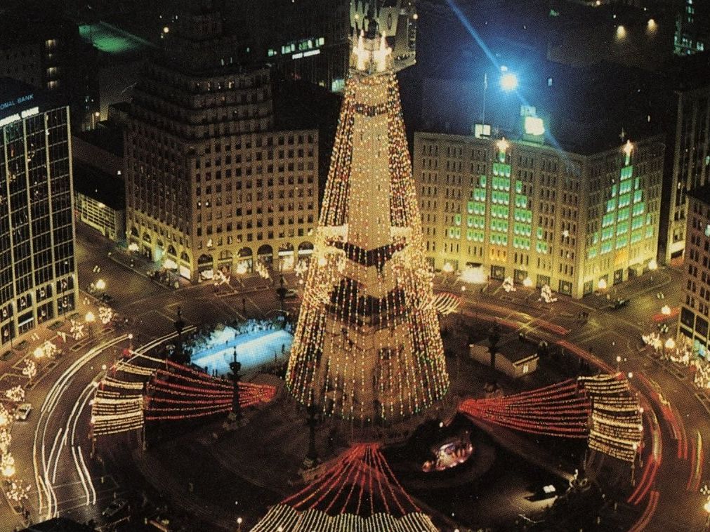 Monument Circle illuminated with holiday lights, featuring the Circle of Lights display surrounded by downtown Indianapolis at night.