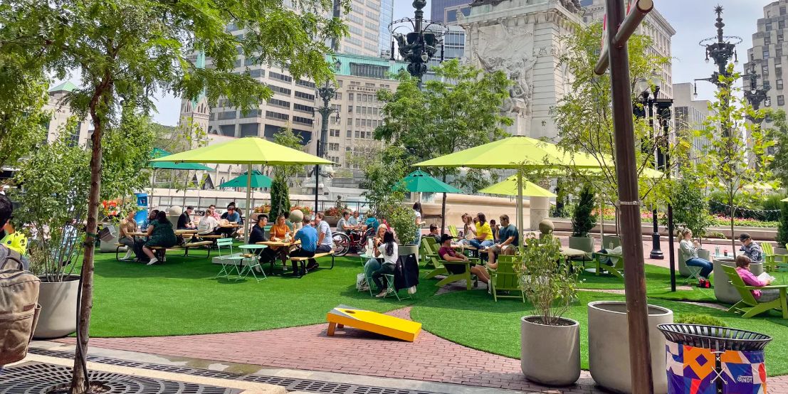 Visitors relax beneath green umbrellas at Spark on the Circle, a vibrant outdoor gathering space surrounding Monument Circle in downtown Indianapolis.