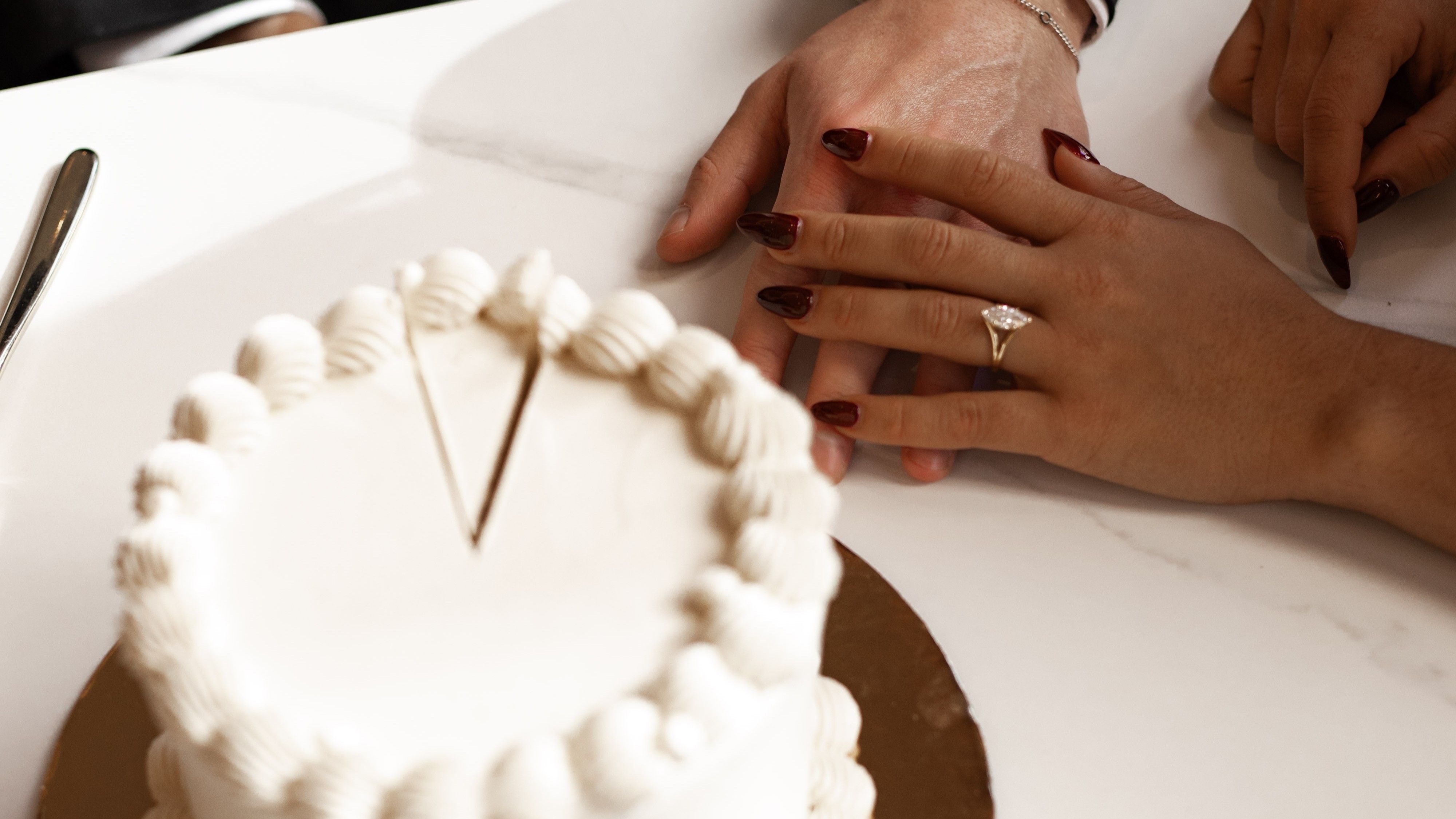 Close up of bride and groom holding hands in front of wedding cake.