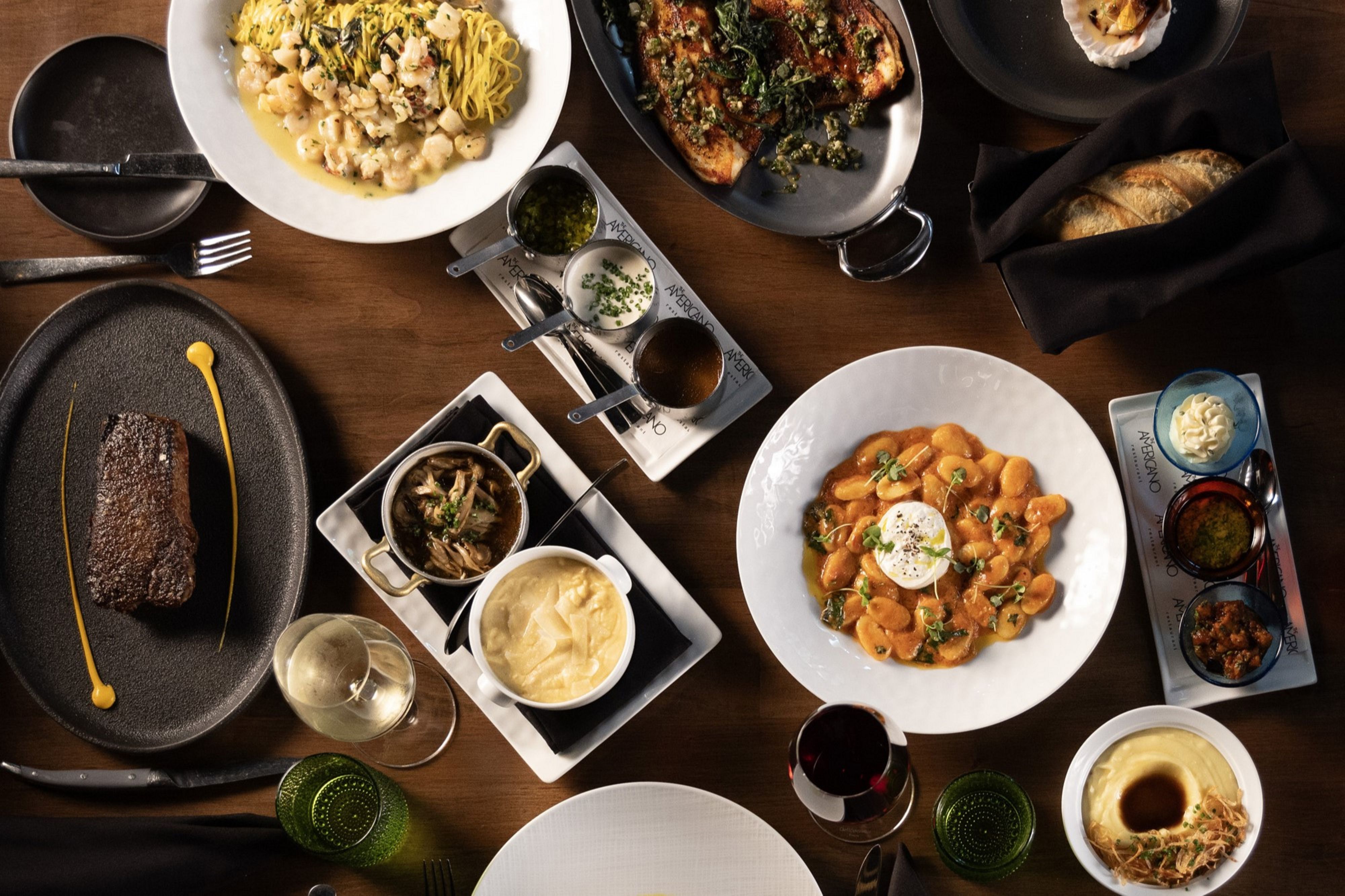 Overhead view of plated dishes, wine, and shared appetizers arranged on a dining table.