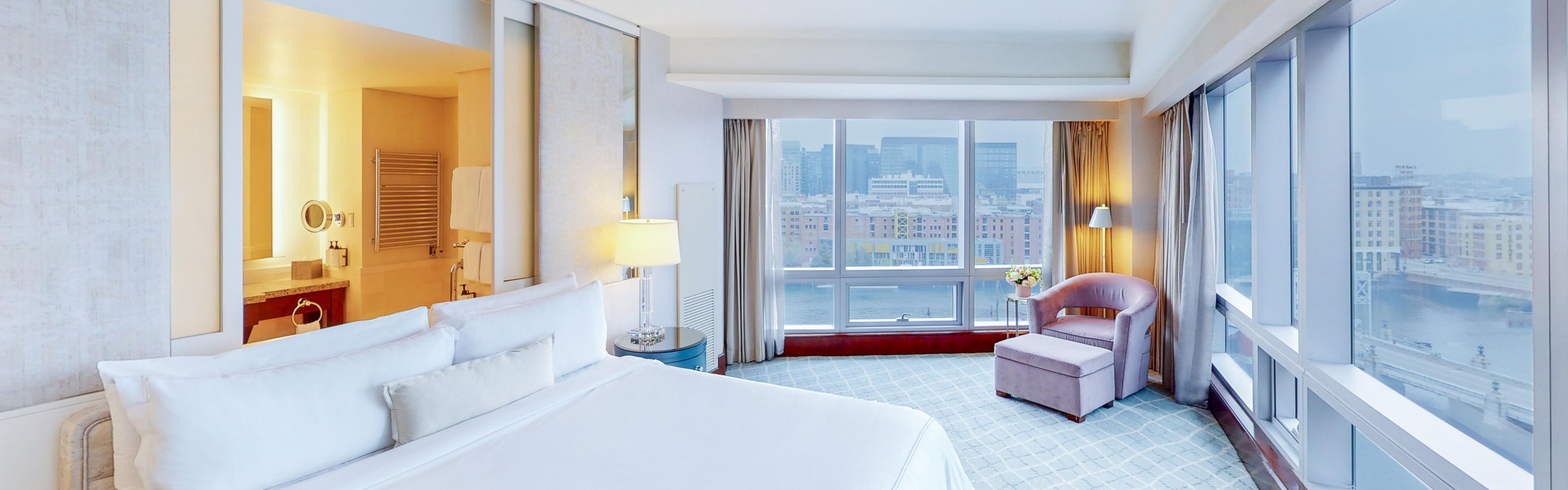 Hotel room with a bed and seating, with city and harbor views.