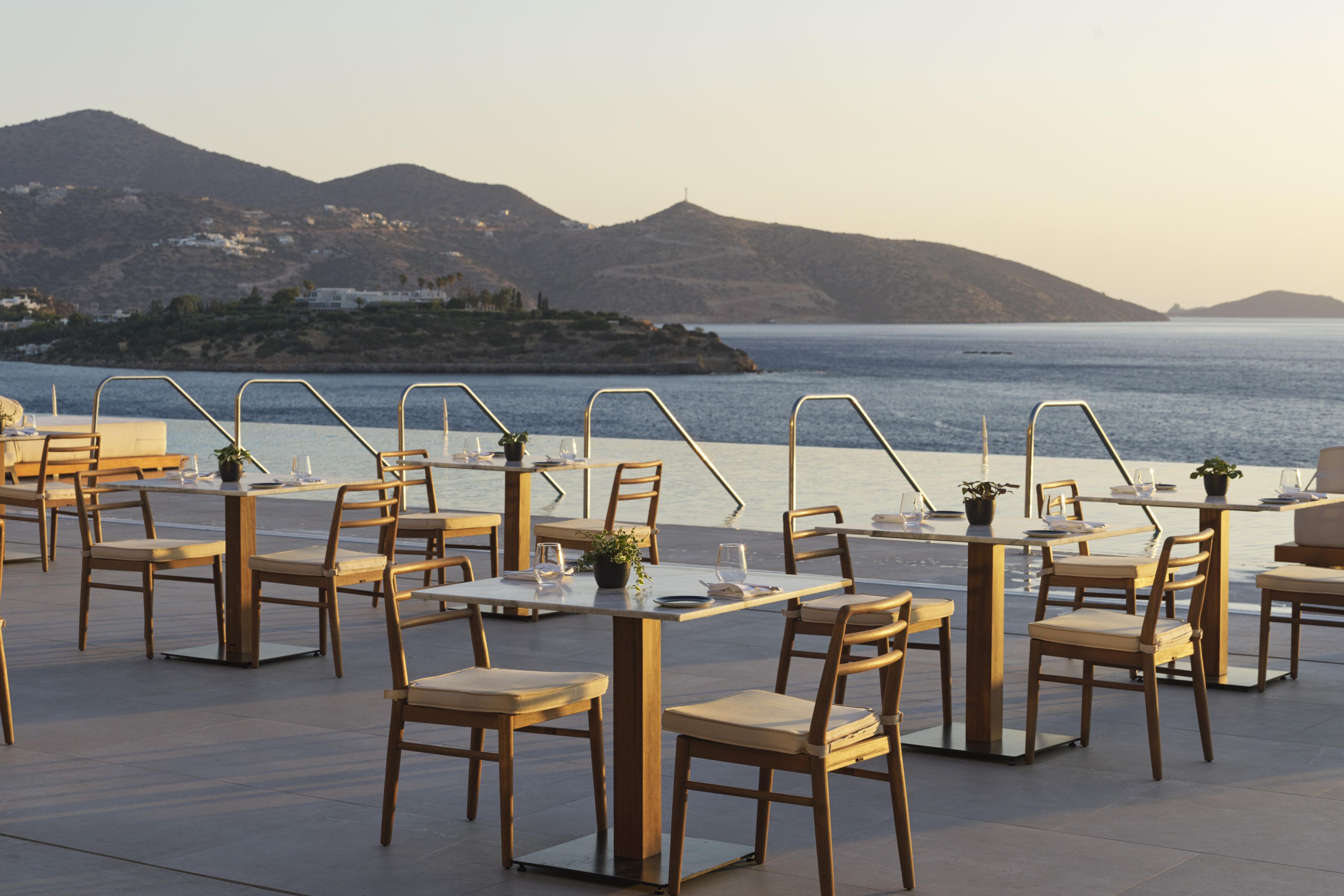 empty tables around the pool with mirabello bay ocean views