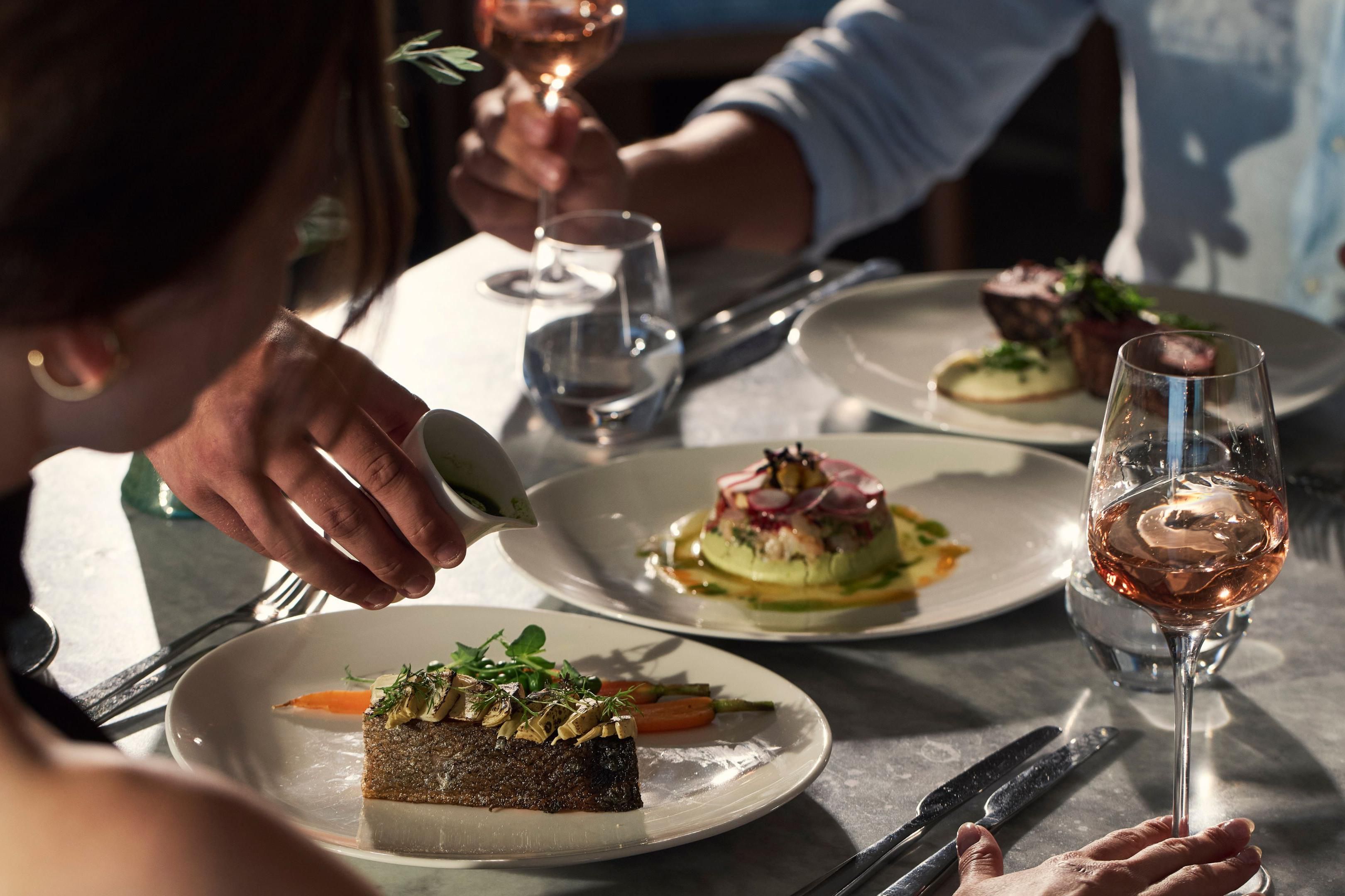 guests eating dinner, table showing various dishes and a glass of rose