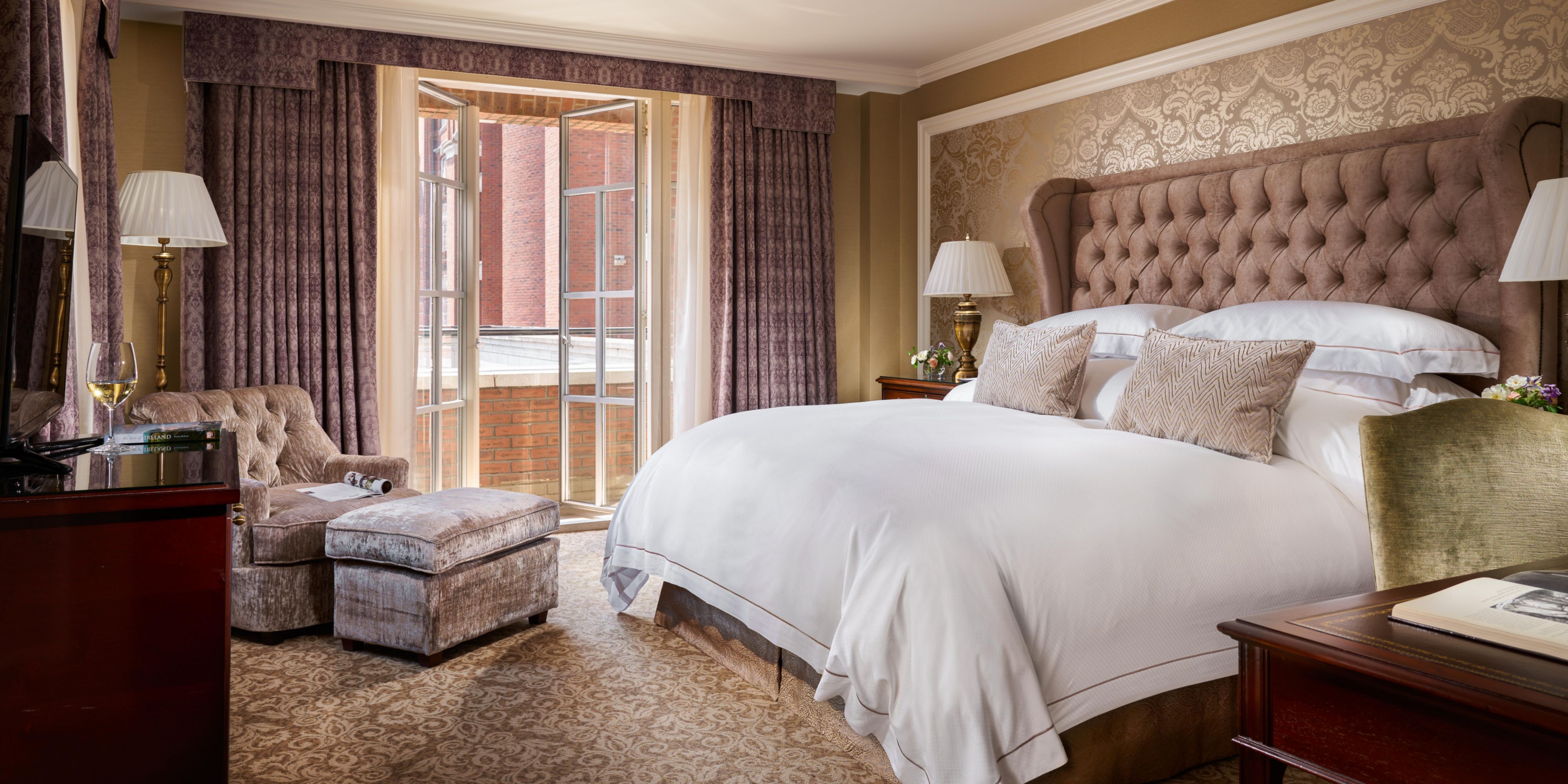 luxury suite featuring a bed, cosy armchair and footrest, and large window